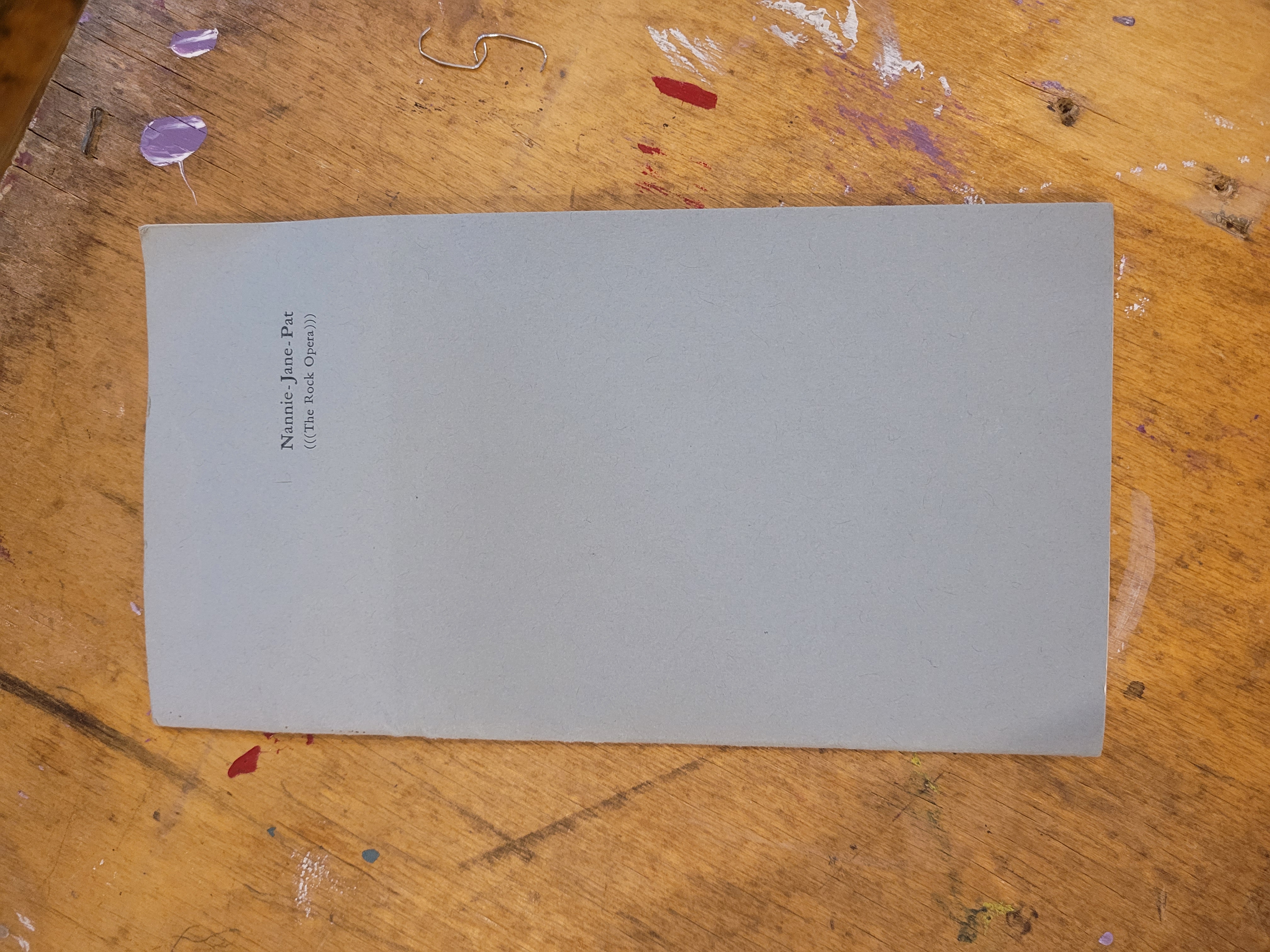 Grey zine cover laying on wooden table. Small text in the upper top right "Nannie-Jane-Pat (((The Rock Opera)))"