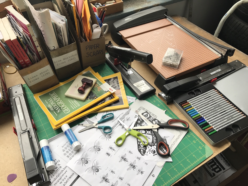 Zine making supplies including clip art, paper cutter, glue sticks, scissors, staplers. 